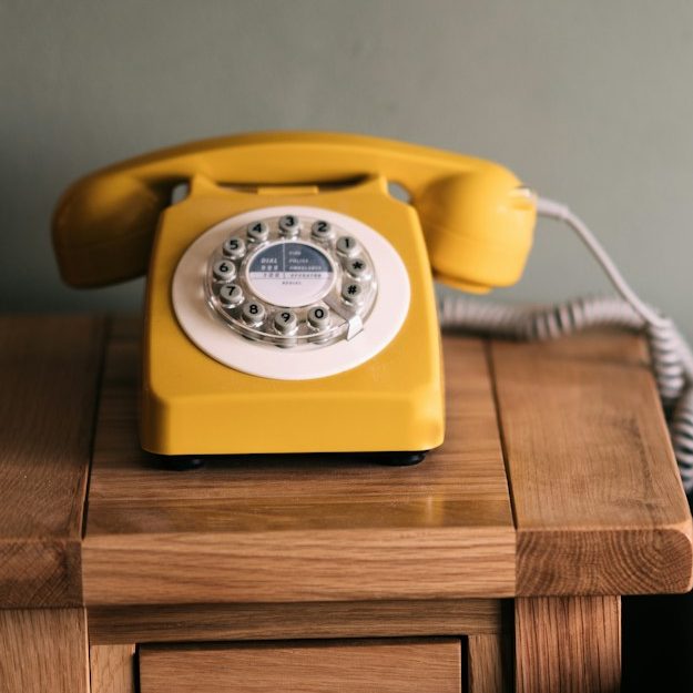 Kontakt Gelbes retro Telefon auf einem Holzschrank.