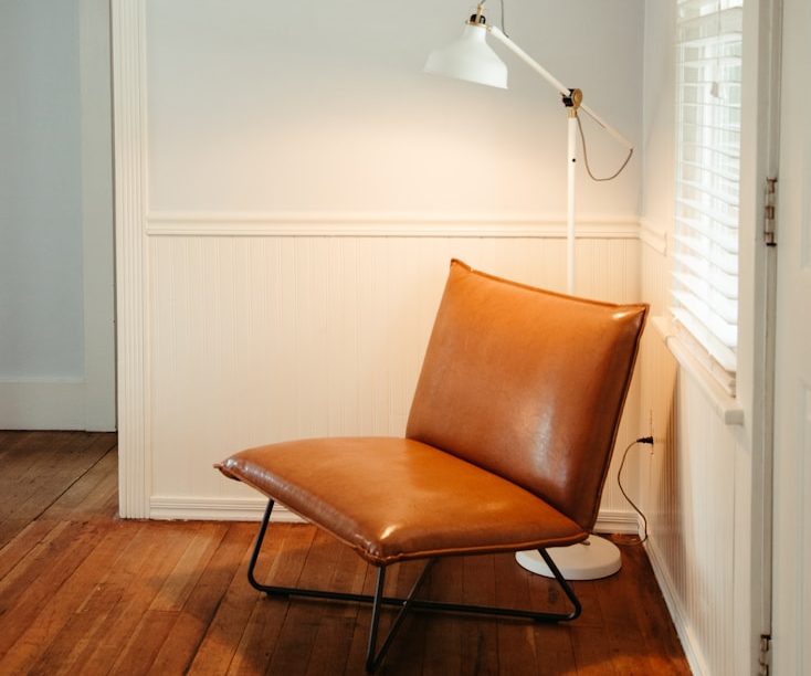 Brauner, moderner Sessel neben einer Lampe in einem hellen Raum mit Holzfußboden.